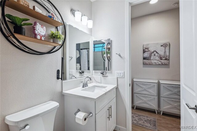 bathroom with toilet, wood finished floors, and vanity