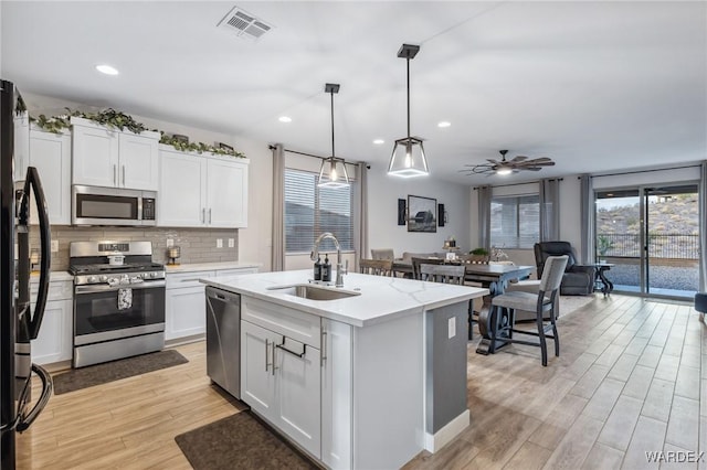 kitchen with an island with sink, appliances with stainless steel finishes, white cabinetry, pendant lighting, and a sink