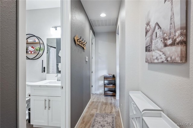 corridor featuring a textured wall, a sink, visible vents, baseboards, and light wood-type flooring