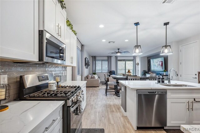 kitchen featuring white cabinets, appliances with stainless steel finishes, open floor plan, and a sink