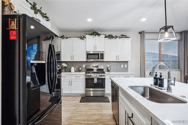 kitchen with light stone counters, stainless steel appliances, white cabinetry, pendant lighting, and a sink