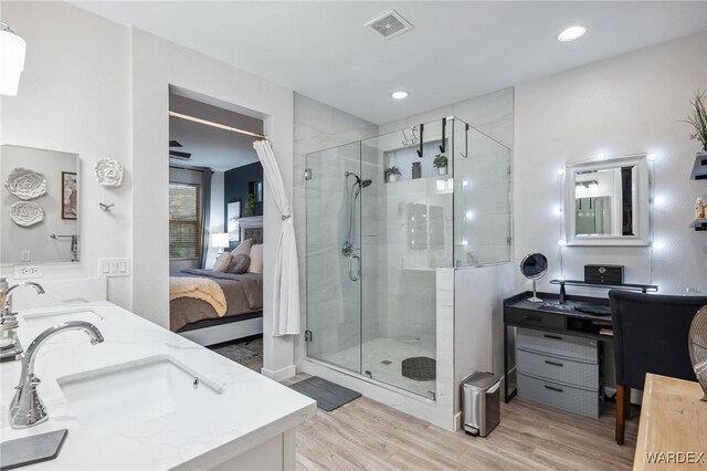 ensuite bathroom featuring double vanity, a stall shower, wood finished floors, ensuite bathroom, and a sink