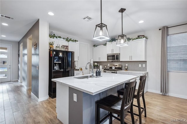 kitchen with visible vents, white cabinets, an island with sink, stainless steel appliances, and a sink