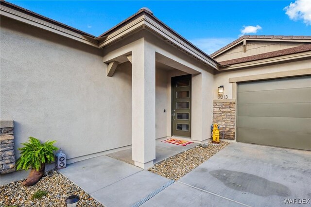 view of exterior entry featuring an attached garage, stone siding, and stucco siding