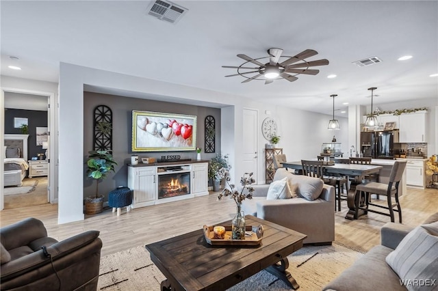 living area featuring a glass covered fireplace, visible vents, and light wood finished floors