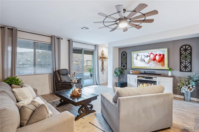 living area with a warm lit fireplace, baseboards, visible vents, and light wood finished floors