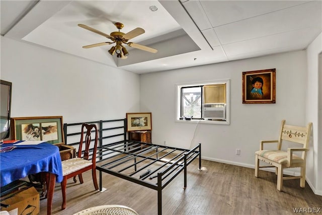 interior space with baseboards, a raised ceiling, ceiling fan, wood finished floors, and cooling unit