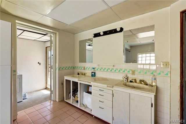 full bath featuring tile walls, double vanity, a sink, a drop ceiling, and tile patterned floors