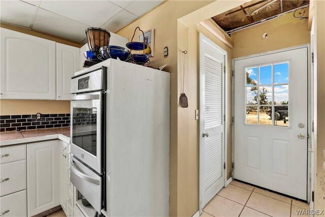 kitchen with light tile patterned floors, tasteful backsplash, fridge, white cabinetry, and a warming drawer