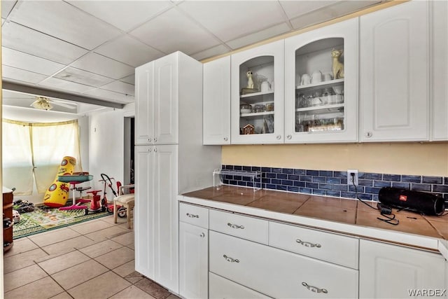 kitchen with a paneled ceiling, glass insert cabinets, white cabinets, and light tile patterned flooring