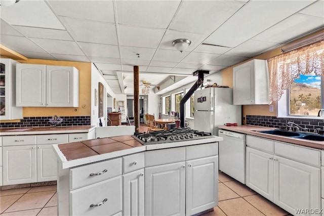 kitchen featuring white appliances, white cabinetry, a sink, and light tile patterned flooring