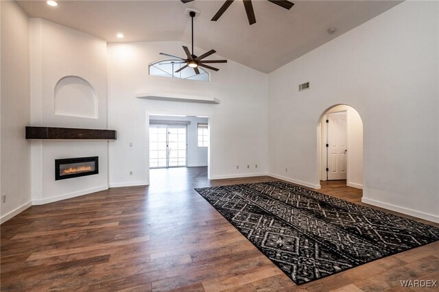 living room with arched walkways, visible vents, a ceiling fan, dark wood-style floors, and a glass covered fireplace