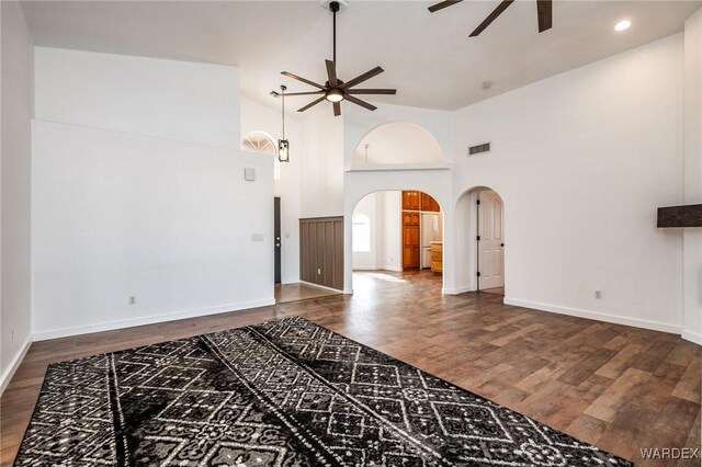 living area featuring baseboards, arched walkways, a ceiling fan, a towering ceiling, and wood finished floors