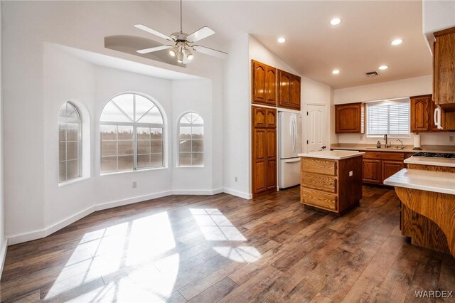 kitchen featuring freestanding refrigerator, a center island, vaulted ceiling, light countertops, and a sink