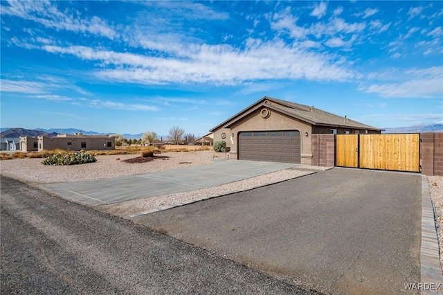 view of side of home featuring driveway, an attached garage, a gate, and stucco siding