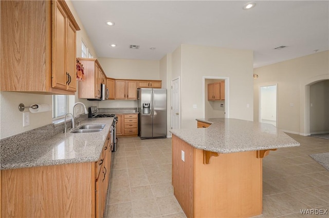 kitchen featuring a kitchen island, light stone counters, stainless steel appliances, a sink, and recessed lighting