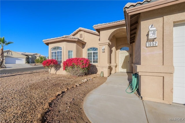 view of exterior entry featuring a garage, a tile roof, and stucco siding