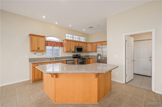 kitchen featuring stainless steel appliances, a sink, a kitchen island, a kitchen breakfast bar, and light stone countertops