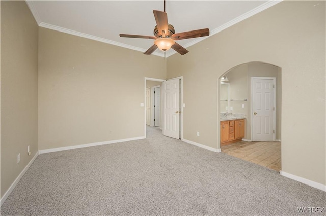 unfurnished bedroom with light carpet, baseboards, arched walkways, connected bathroom, and crown molding