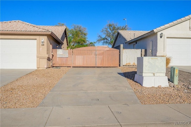 view of side of home featuring driveway, a tiled roof, a gate, and stucco siding