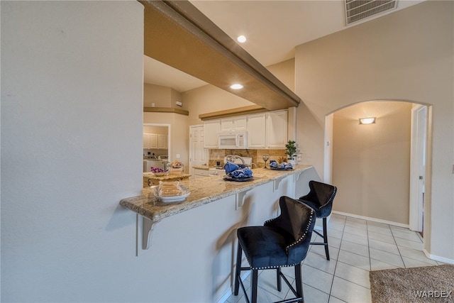 kitchen with white microwave, visible vents, tasteful backsplash, stove, and arched walkways