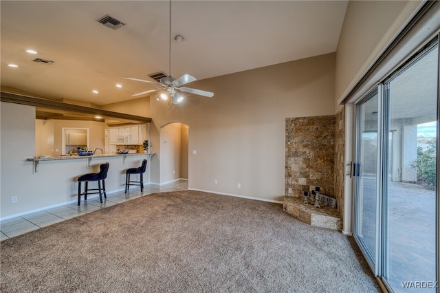 unfurnished living room featuring light tile patterned floors, visible vents, arched walkways, ceiling fan, and light colored carpet