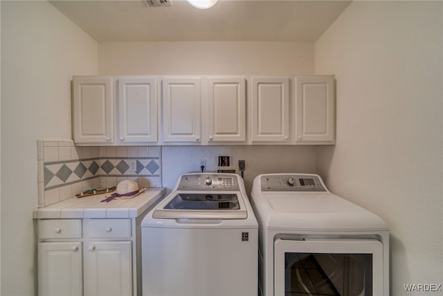 washroom with washer and dryer, cabinet space, and visible vents