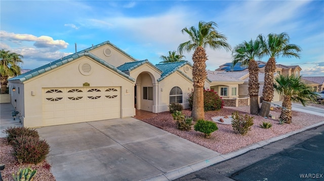 view of front of property with a tiled roof, stucco siding, an attached garage, and driveway