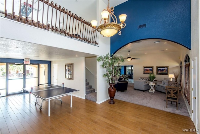 rec room with visible vents, ceiling fan with notable chandelier, a towering ceiling, wood finished floors, and arched walkways