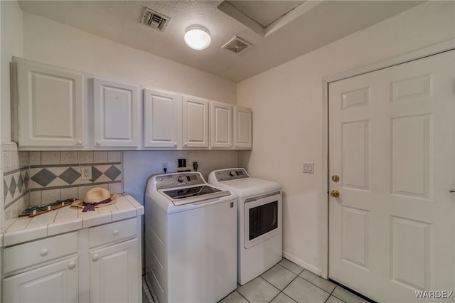 laundry area with separate washer and dryer, light tile patterned floors, cabinet space, and visible vents