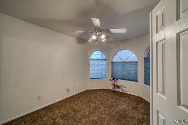 empty room with baseboards, ceiling fan, and dark carpet