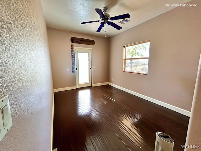 empty room with a ceiling fan, baseboards, visible vents, dark wood finished floors, and a textured wall