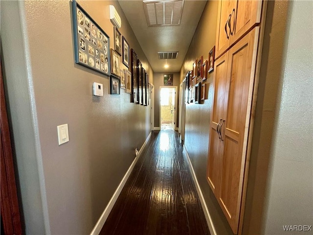 corridor with dark wood-style floors, visible vents, and baseboards