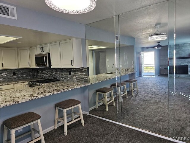 1800 Clubhouse Dr Unit 89, Bullhead City, AZ 86442 - kitchen featuring stainless steel microwave, tasteful backsplash, dark colored carpet, visible vents, and range with electric stovetop