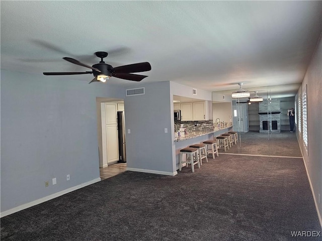 1800 Clubhouse Dr Unit 89, Bullhead City, AZ 86442 - unfurnished living room with dark colored carpet, baseboards, a fireplace, visible vents, and ceiling fan