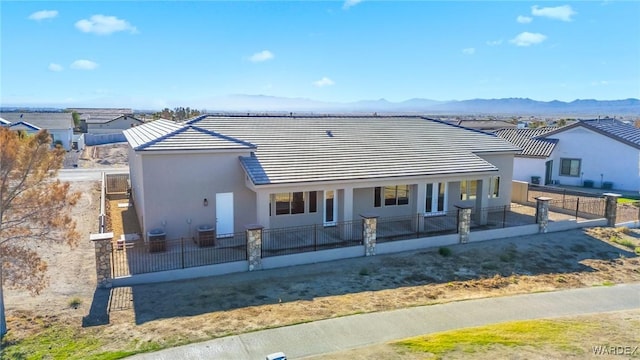 view of front of home featuring a fenced front yard, a mountain view, central AC, a tiled roof, and stucco siding