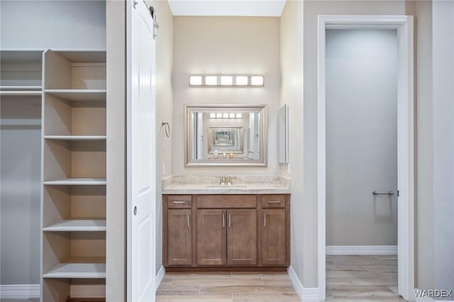 bathroom featuring vanity, baseboards, a closet, and wood finish floors