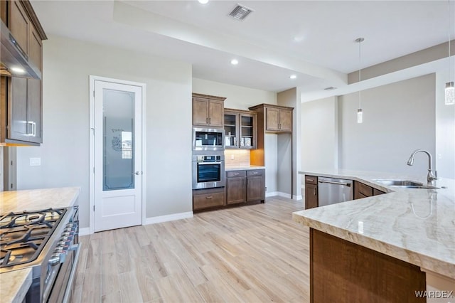 kitchen featuring decorative light fixtures, stainless steel appliances, glass insert cabinets, a sink, and light stone countertops