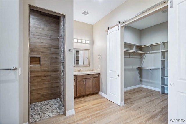 full bathroom featuring a tile shower, a spacious closet, vanity, and wood finished floors