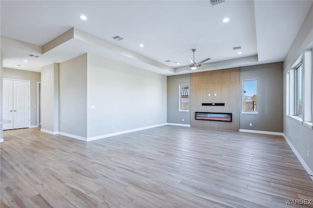 unfurnished living room featuring light wood-type flooring, a fireplace, a raised ceiling, and baseboards