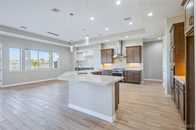 kitchen with tasteful backsplash, visible vents, wall chimney exhaust hood, hanging light fixtures, and light stone countertops