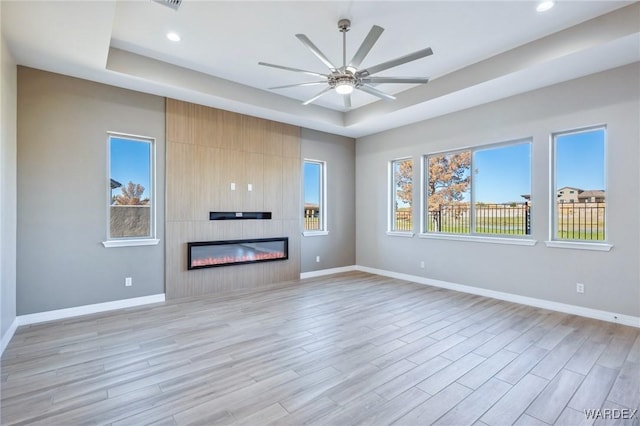 unfurnished living room with a tray ceiling, a fireplace, light wood-style flooring, and baseboards