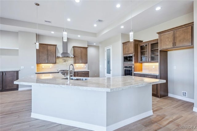 kitchen featuring a large island, stainless steel appliances, hanging light fixtures, a sink, and wall chimney exhaust hood