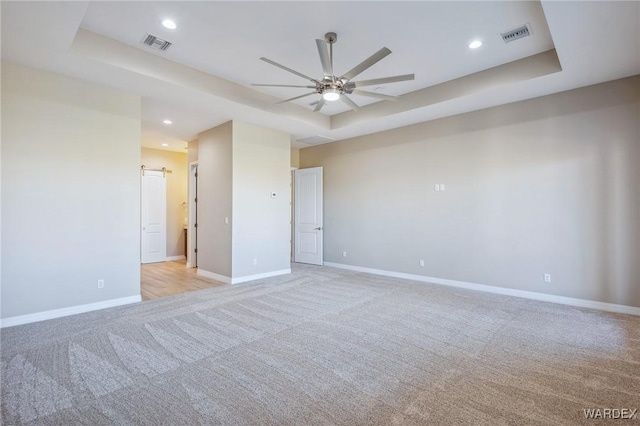 empty room with a tray ceiling, recessed lighting, visible vents, light carpet, and baseboards