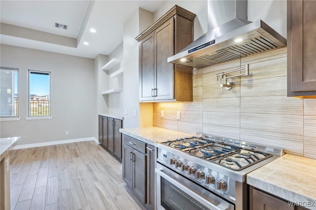 kitchen with light wood finished floors, visible vents, high end range, wall chimney range hood, and backsplash