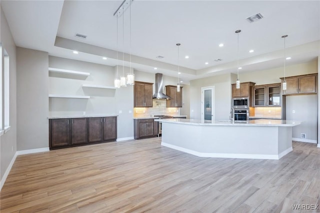 kitchen featuring pendant lighting, a spacious island, visible vents, appliances with stainless steel finishes, and wall chimney range hood