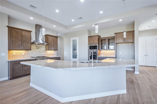 kitchen featuring visible vents, wall chimney exhaust hood, a large island, appliances with stainless steel finishes, and hanging light fixtures