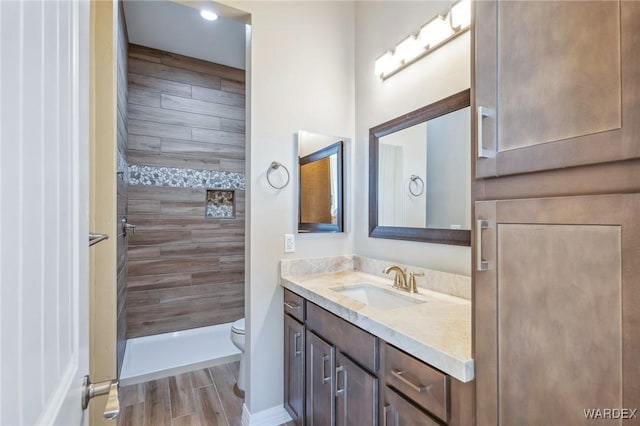 full bathroom with tiled shower, vanity, toilet, and wood finished floors