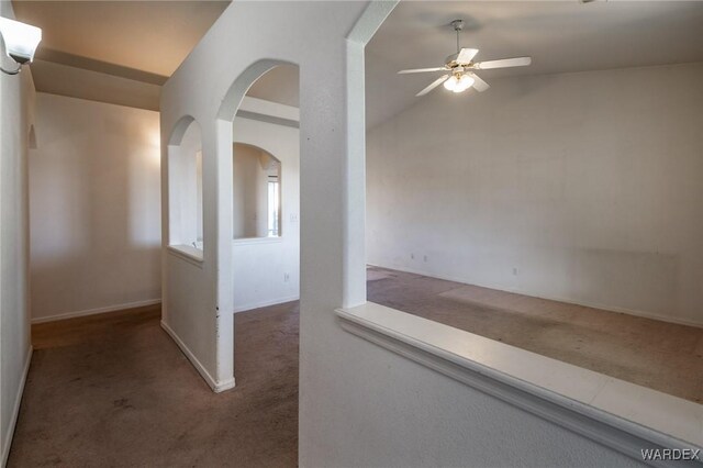 hall featuring carpet floors, arched walkways, vaulted ceiling, and baseboards