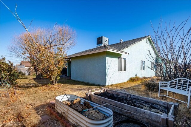 rear view of house featuring central air condition unit, a shingled roof, a vegetable garden, and stucco siding